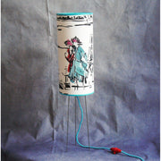 Lampe à poser abat-jour cylindrique sue trépied, papier peint Manuel Canovas.